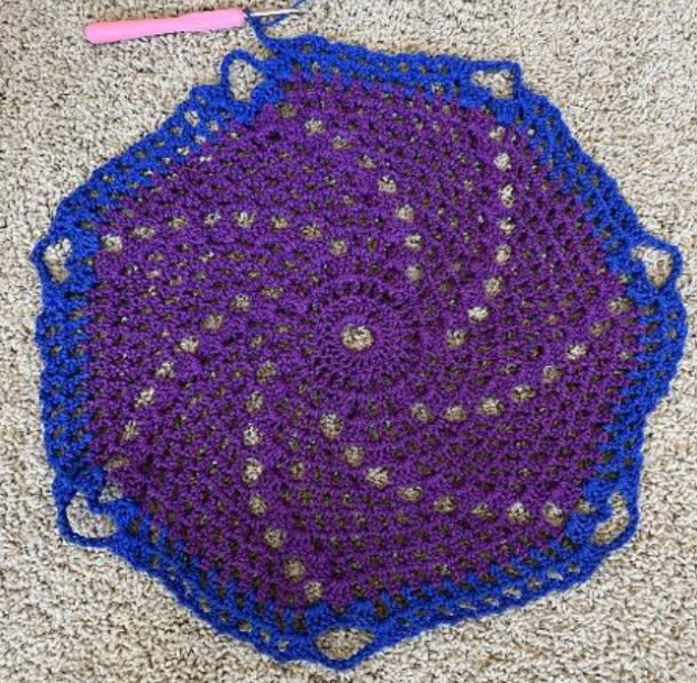 el mismo proyecto de crochet en espiral morado que muestra un mayor progreso con una capa azul alrededor del exterior