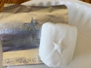 photo of a marshmallow with a raised star on the surface, in front of a piece of aluminum with the same star shape cut out of the center
